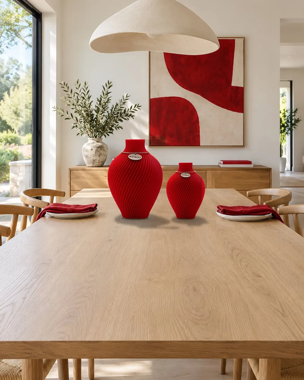 Two empty Fire Red Noma vases of different heights on a timber dining table, near an artwork with red shapes